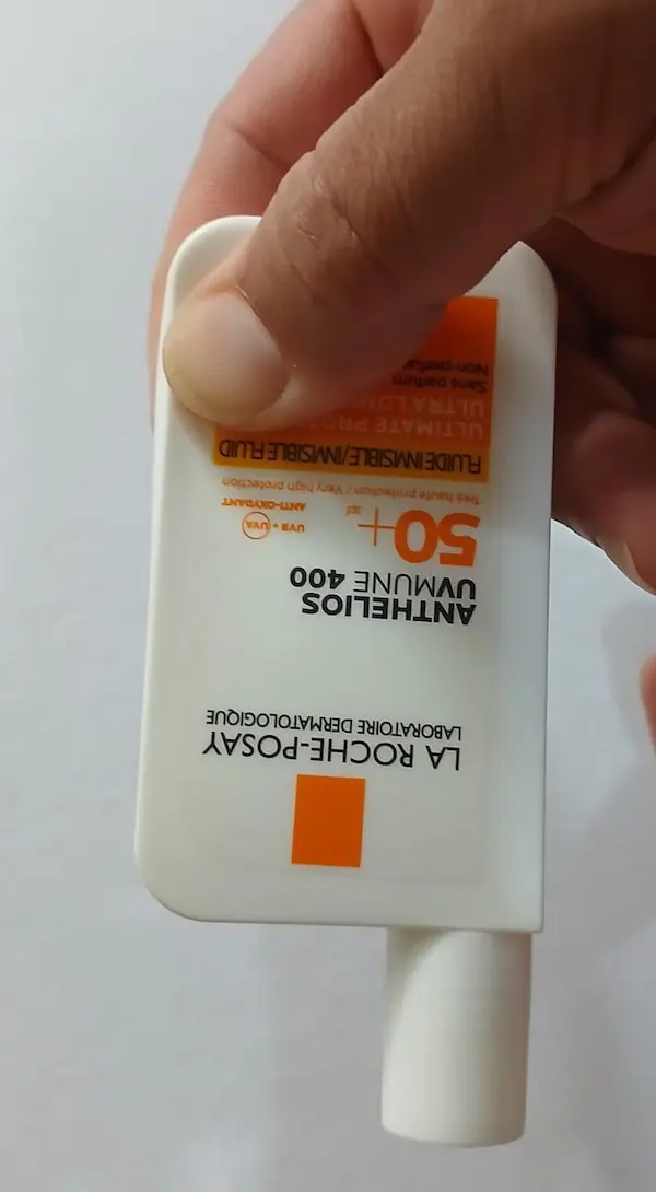 Fake La Roche-Posay Anthelios sunscreen bottle being pressed at the bottom corner with one thumb, the hard stiff plastic does not move outward