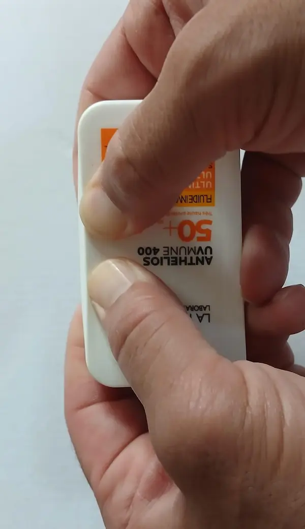 Fake La Roche-Posay Anthelios sunscreen bottle being pressed near the edges with both thumbs, the hard stiff plastic does not move outward
