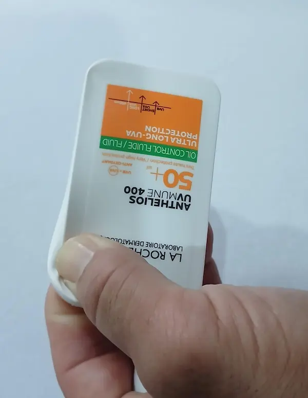 Original La Roche-Posay Anthelios Oil Control sunscreen bottle being pressed at the top corner with one thumb, showing the soft flexible plastic of a genuine bottle