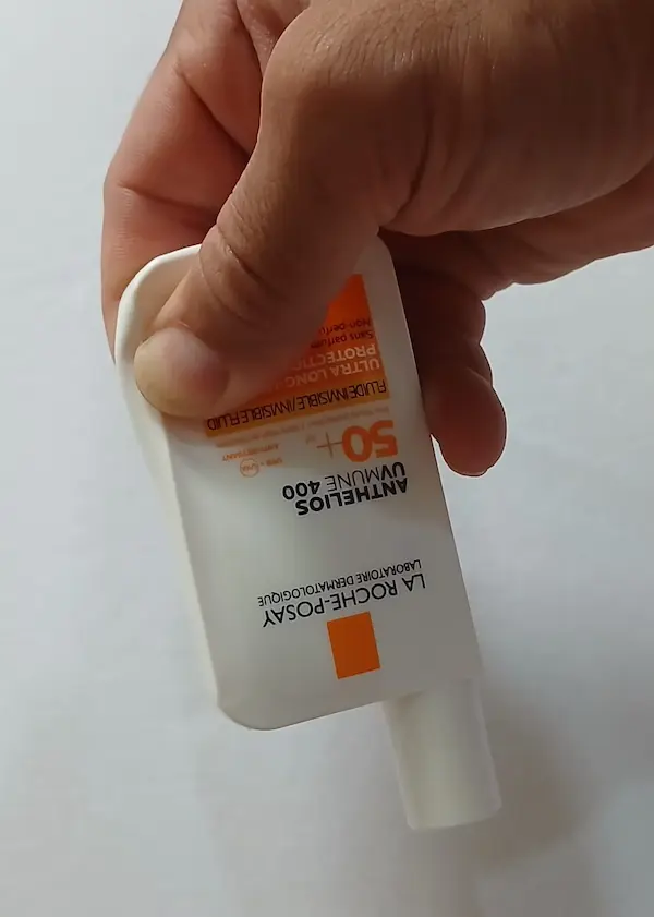 Original La Roche-Posay Anthelios sunscreen bottle being pressed at the bottom corner with one thumb, showing the soft flexible plastic of a genuine bottle