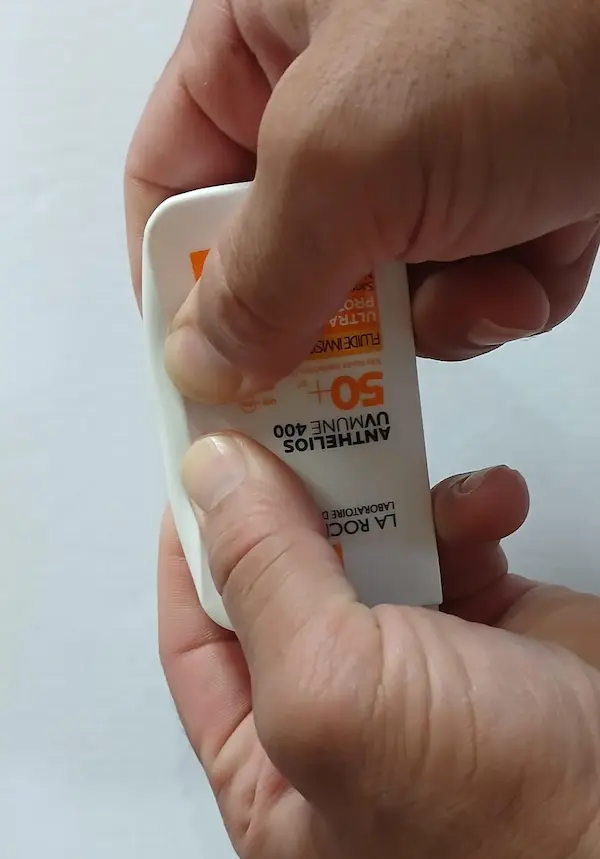 Original La Roche-Posay Anthelios sunscreen bottle being pressed near the edges with both thumbs, showing the soft flexible plastic of a genuine bottle