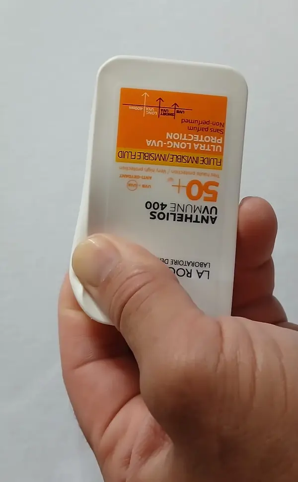 Original La Roche-Posay Anthelios sunscreen bottle being pressed at the top corner with one thumb, showing the soft flexible plastic of a genuine bottle